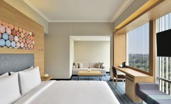 a modern hotel room with a white bed , wooden desk , and large window offering a view of the city at Aloft New Delhi Aerocity