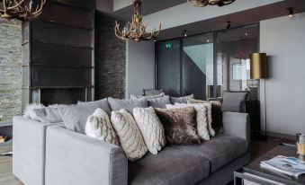 a gray couch with multiple pillows is in a room with a chandelier and large windows at Langley Hotel Tignes 2100