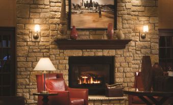 a cozy living room with a brick fireplace , red leather chairs , and a painting on the wall at DoubleTree by Hilton Hotel Cincinnati Airport