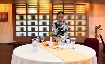 a woman is standing behind a dining table set with various items , including water bottles , cups , and utensils at Asana Biak Papua Hotel