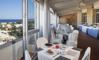 a dining room with a table set for a meal , surrounded by white chairs and large windows at Hotel Tirreno
