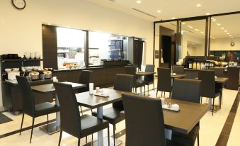 a modern restaurant with black tables and chairs , white walls , and large windows , offering a view of the kitchen at Dormy Inn Mishima