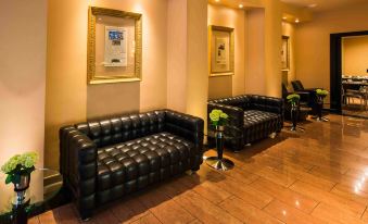 a black leather couch and chair in a room with gold framed pictures on the wall at Hotel Concorde