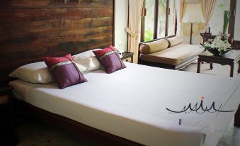 a bed with white sheets and purple pillows is in a room with a wooden headboard at Parn Dhevi Riverside Resort & Spa