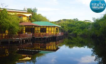 a yellow building on stilts over a body of water , surrounded by lush greenery and trees at Hotel Estero y Mar