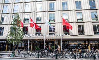 a group of people are standing outside a building with flags and bicycles parked outside at Scandic Falkoner