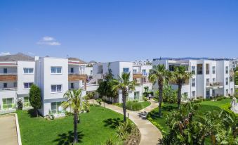 a beautiful apartment complex with white buildings , surrounded by lush green grass and palm trees , under a clear blue sky at Armonia Holiday Village & Spa
