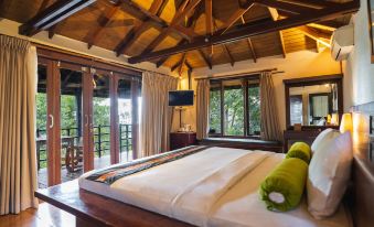 a large bed with a white sheet and green pillows is in a room with wooden walls and floors at Horison Green Forest Bandung