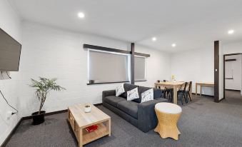 a modern living room with a couch , dining table , and chairs arranged around it , as well as a television mounted on the wall at Scamander Beach Resort