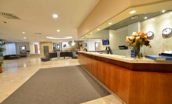 a modern hotel reception area with a large wooden counter , two chairs , and a vase of flowers at Best Western Park Hotel