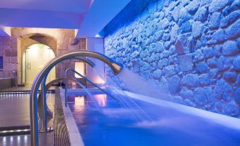 a large indoor swimming pool with a waterfall feature , surrounded by stone walls and lit up at night at Parador de Santo Estevo
