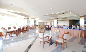 a large dining room with wooden chairs and tables , a buffet table , and a television at Grand Elty Singgasana Hotel