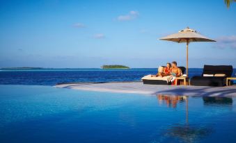 a couple is relaxing on a lounge chair by the ocean , with an umbrella providing shade at Komandoo Island Resort & Spa