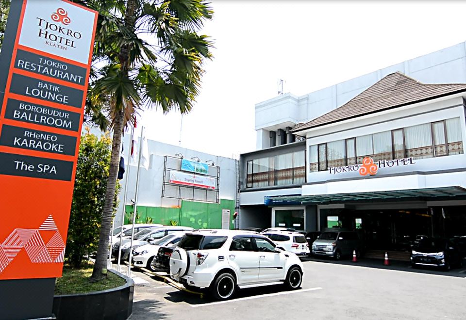 a white car is parked in a parking lot with other cars and a building with a palm tree at Tjokro Hotel Klaten