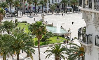 a city square with palm trees , a fountain , and people walking around , surrounded by buildings and balconies at Okko Hotels Toulon Centre