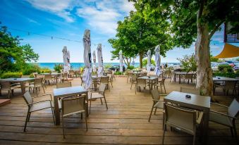 a wooden deck overlooking the ocean , with tables and chairs set up for outdoor dining at Hotel Opal