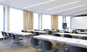 a large conference room with multiple rows of chairs arranged in a semicircle , and a projector on the wall at Novotel Freiburg am Konzerthaus
