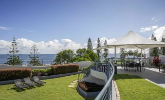 a large backyard with a grassy area and a view of the ocean , featuring a gazebo , lounge chairs , and a slide at Mantra Mooloolaba Beach