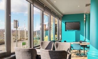a modern living room with large windows , blue and green walls , and gray furniture arranged around a coffee table at Holiday Inn Leeds - Brighouse