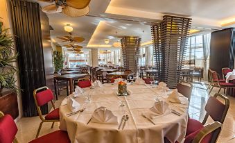 a large dining room with multiple tables set for a formal dinner , featuring a white tablecloth and red chairs at Amazonia Jamor Hotel