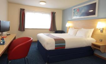 a large bed with a colorful blanket is in a hotel room with blue carpet at Travelodge Glenrothes