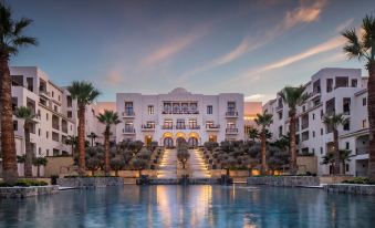 a large white building with a staircase leading up to it , surrounded by palm trees and a pool at Four Seasons Hotel Tunis