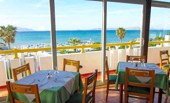 a restaurant with a view of the ocean has tables and chairs set up for dining at Mastichari Bay Hotel