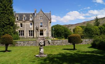 a large stone house surrounded by a lush green lawn , with a statue in the middle of the yard at Glengarry Castle Hotel