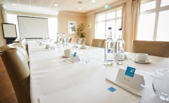 a long table is set with water bottles , glasses , and name tags in a conference room at Trearddur Bay Hotel