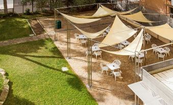 a patio area with several tables and chairs under a large tent , surrounded by grass and trees at Bluesea Costa Verde