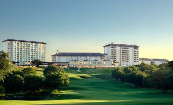 a golf course with a large building in the background , surrounded by trees and grass at Omni Barton Creek Resort and Spa Austin