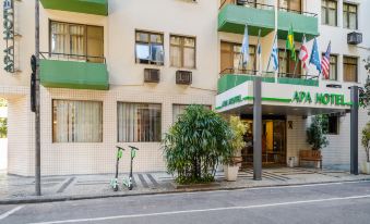 a building with green and white flags flying , trees , and parked scooters on the sidewalk at Infinity Copacabana, Ex-APA Hotel