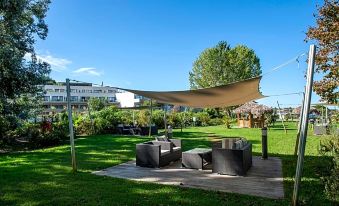 a patio area with a wooden deck , black chairs and a large beige canopy , surrounded by green grass and trees at Suite Home Porticcio
