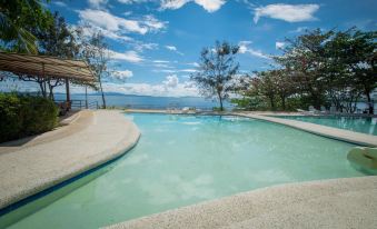 a large outdoor swimming pool surrounded by trees , with a view of the ocean in the background at Almont Beach Resort
