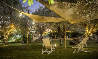 a well - lit outdoor area with a dining table , chairs , and an umbrella , surrounded by trees and grass at Smy Civico Zero