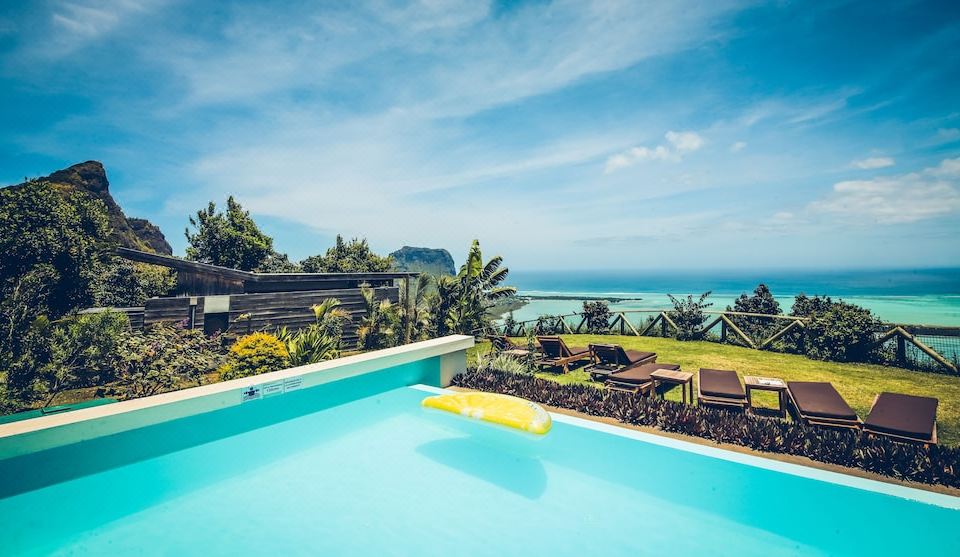 a large swimming pool with a yellow lounge chair and lounge area in front of the ocean at Chalets Chamarel