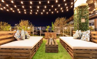 a well - lit outdoor space with wooden benches and a large table , under string lights and string lights at Mercure Melbourne Caroline Springs