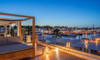 a beautiful outdoor setting with a wooden deck , lit by lanterns , overlooking a harbor at dusk at Lago Resort Menorca Casas del Lago