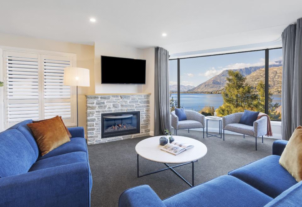 a modern living room with blue couches and chairs arranged around a fireplace , creating a cozy atmosphere at Oaks Queenstown Shores Resort
