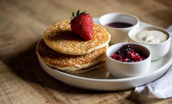 a plate of pancakes topped with strawberries and served on a wooden table , accompanied by a bowl of fruit at The Seven Stars