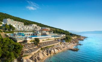 a beautiful coastal resort with a pool , white buildings , and clear blue skies , surrounded by cliffs and trees at Valamar Bellevue Resort