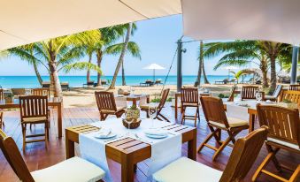 an outdoor dining area with wooden tables , chairs , and umbrellas , surrounded by palm trees and a beautiful ocean view at Small Luxury Hotels of the World - Sublime Samana Hotel & Residences