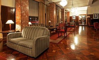 a large , well - lit room with wooden floors and marble walls , containing a variety of seating options such as couches and chairs at Hotel Astoria