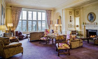 a luxurious living room with a large window , purple carpet , and floral chairs around a coffee table at Bovey Castle