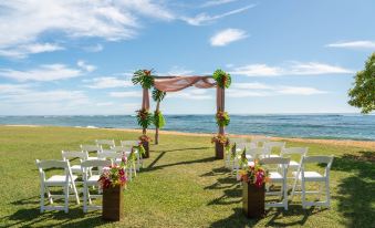 a wedding ceremony is taking place on a grassy field near the ocean , with rows of white chairs set up for guests at Sheraton Kauai Coconut Beach Resort