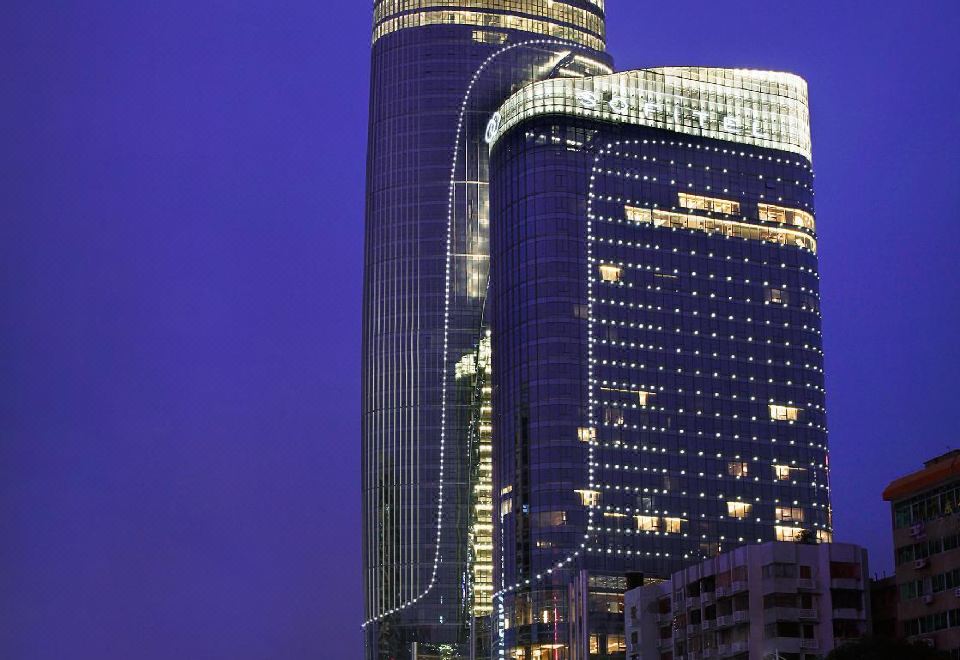 At night, a cityscape is illuminated by a large building with numerous windows, which includes an office tower at Sofitel Guangzhou Sunrich