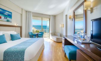 a modern hotel room with a large window offering an ocean view , wooden flooring , and blue accent chairs at Golden Bay Beach Hotel