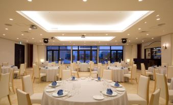 a large , well - lit banquet hall with multiple round tables set for a formal event , white tablecloths , and a view of at Hotel Kanazawa