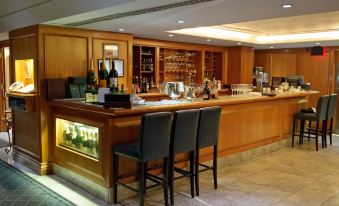 a well - lit bar area with a wooden counter and two black chairs , surrounded by various bottles and wine glasses at The Waterside Inn