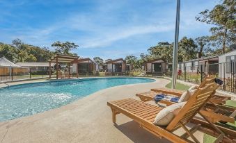 a large swimming pool with a wooden deck and lounge chairs in front of a house at Reflections Jimmys Beach - Holiday Park